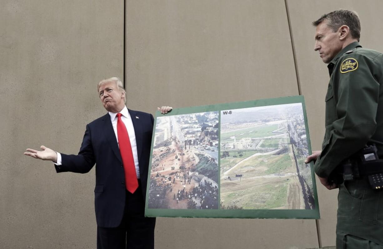 FILE - In this March 13, 2018, file photo, President Donald Trump holds a poster with photographs of the U.S. - Mexico border area as he reviews border wall prototypes in San Diego with Rodney Scott, the U.S. Border Patrol’s San Diego sector chief. U.S. District Judge Haywood Gilliam Jr. has blocked President Donald Trump from building sections of his long-sought border wall with money secured under his declaration of a national emergency, Friday, May 24, 2019.