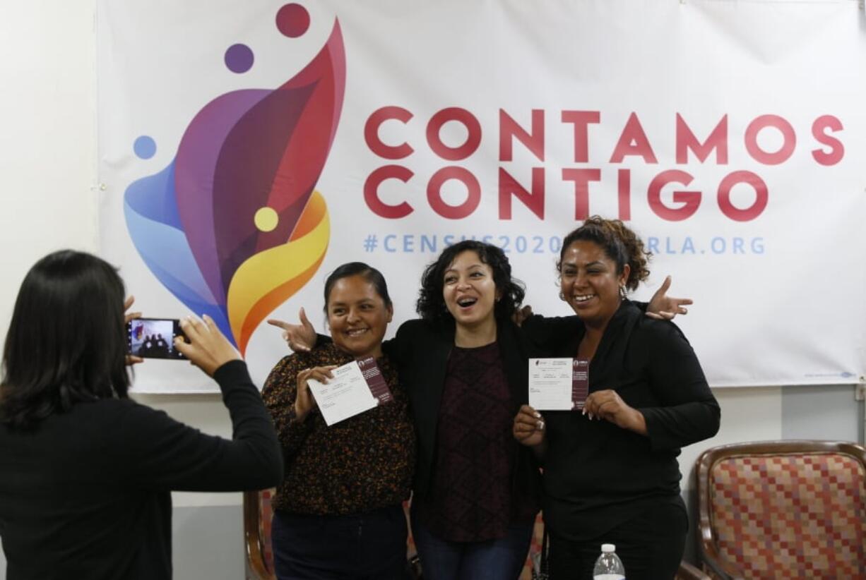 In this Friday, April 26, 2019, photo, Esperanza Guevara, with the Coalition for Humane Immigrant Rights, left, snaps a picture in front of a census campaign poster of volunteers Angeles Rosales, second from left, Janet Mendez, right, and organizer Diana Escamilla at their office in Los Angeles. States are spending millions of dollars on outreach and promotion, connecting with nonprofits and working with cities in an effort to ensure that as many of their residents as possible are counted in the upcoming census.