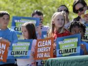 Children hold signs as they stand on stage with Washington Gov. Jay Inslee, who signed bills addressing climate change, Tuesday, May 7, 2019, in Seattle.
