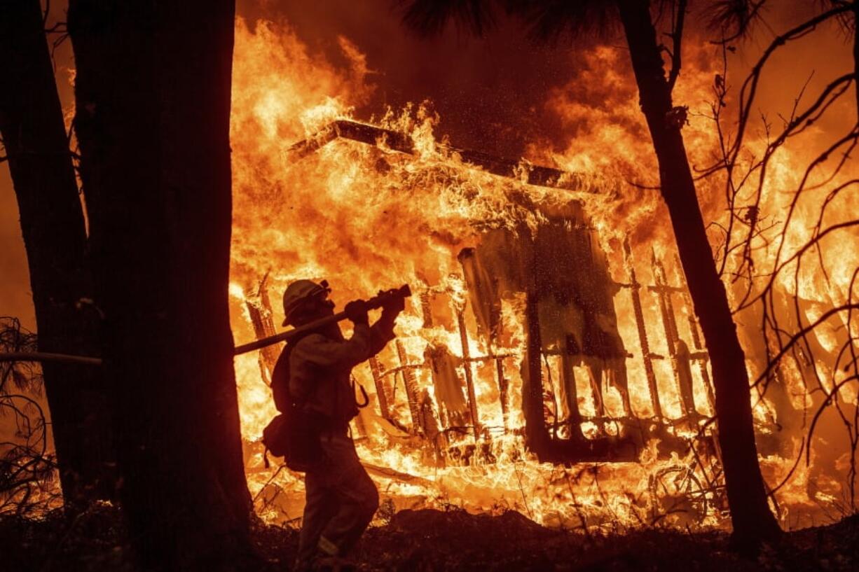 FILE - In this Nov. 9, 2018 file photo, firefighter Jose Corona sprays water as flames from the Camp Fire consume a home in Magalia, Calif. Federal officials say an effort to develop a better fire shelter following the deaths of 19 wildland firefighters in Arizona six years ago has failed. Officials at the National Interagency Fire Center in Boise in a decision on Wednesday, May 15, 2019 say the current fire shelter developed in 2002 will remain in use, saying the current shelter combines the most practical level of protection balanced against weight, bulk and durability.