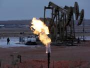 FILE - In this Oct. 22, 2015 file photo, workers tend to oil pump jacks behind a natural gas flare near Watford City, N.D. Natural gas is being burned off and wasted at record levels in North Dakota because development of the pipelines and processing facilities needed to handle it has not kept pace. Natural gas production hit a record in March. But about 20 percent of it went up in flames through “flaring,” the process of burning off the gas when it can’t be captured.