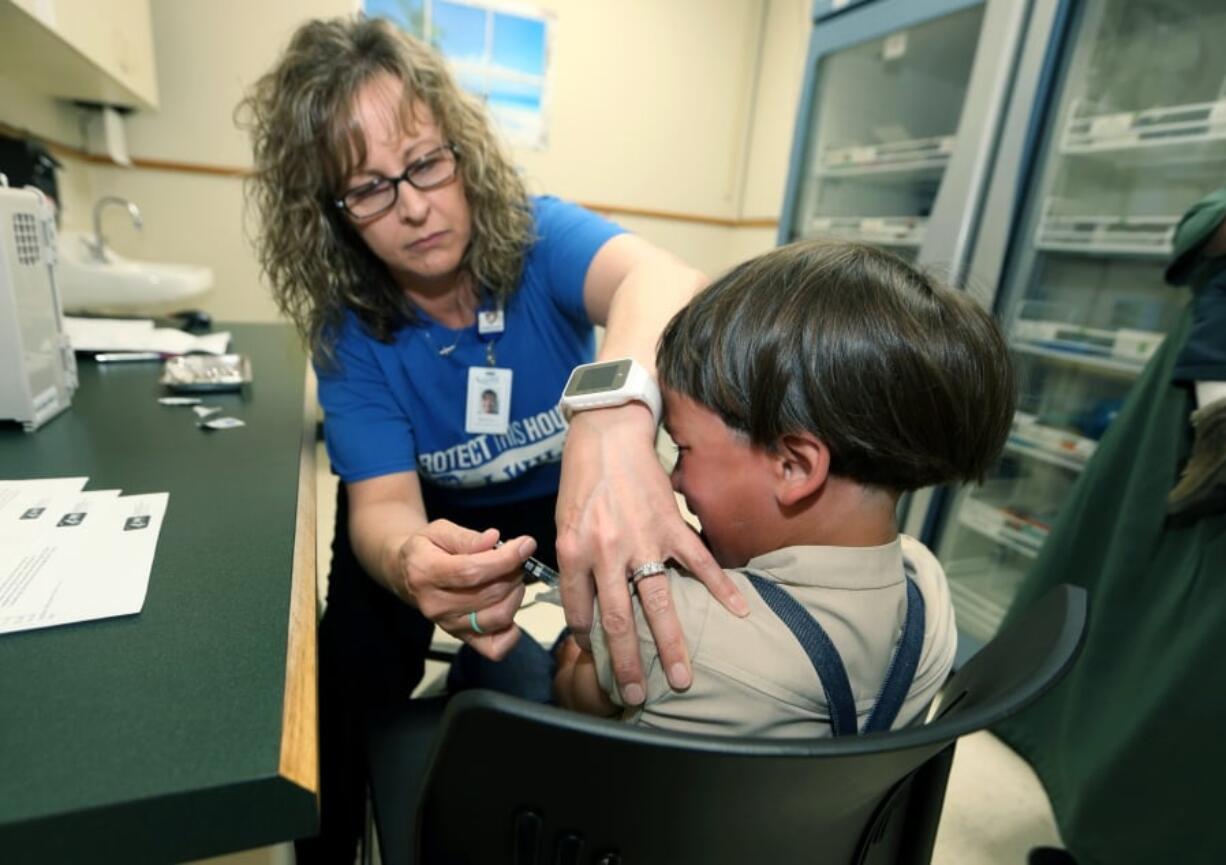 In this Friday, May 17, 2019 photo, Starr Roden, left, a registered nurse and immunization outreach coordinator with the Knox County Health Department, administers a vaccination to Jonathan Detweiler, 6, at the facility in Mount Vernon, Ohio. States are debating whether to make it more difficult for students to avoid vaccinations for religious or philosophical reasons amid the worst measles outbreak in decades, but children using such waivers are outnumbered in many states by those who give no excuse for lacking shots.Data reported to the Centers for Disease Control and Prevention shows a majority of unvaccinated or undervaccinated kindergartners in 10 of 27 states reporting were allowed to enroll in school without any exemption.