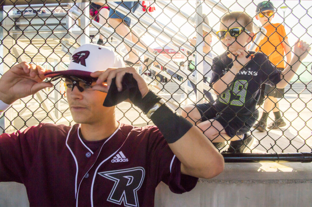 Jude Amundsen, 4, whose family is hosting a Raptors’ player, peers over the shoulder of Ridgefield’s Wyatt Hoffman while the team prepares for the first pitch on opening day Tuesday at the new Ridgefield Outdoor Recreation Complex. The team played their first home game Tuesday night in their inaugural season in the West Coast League.