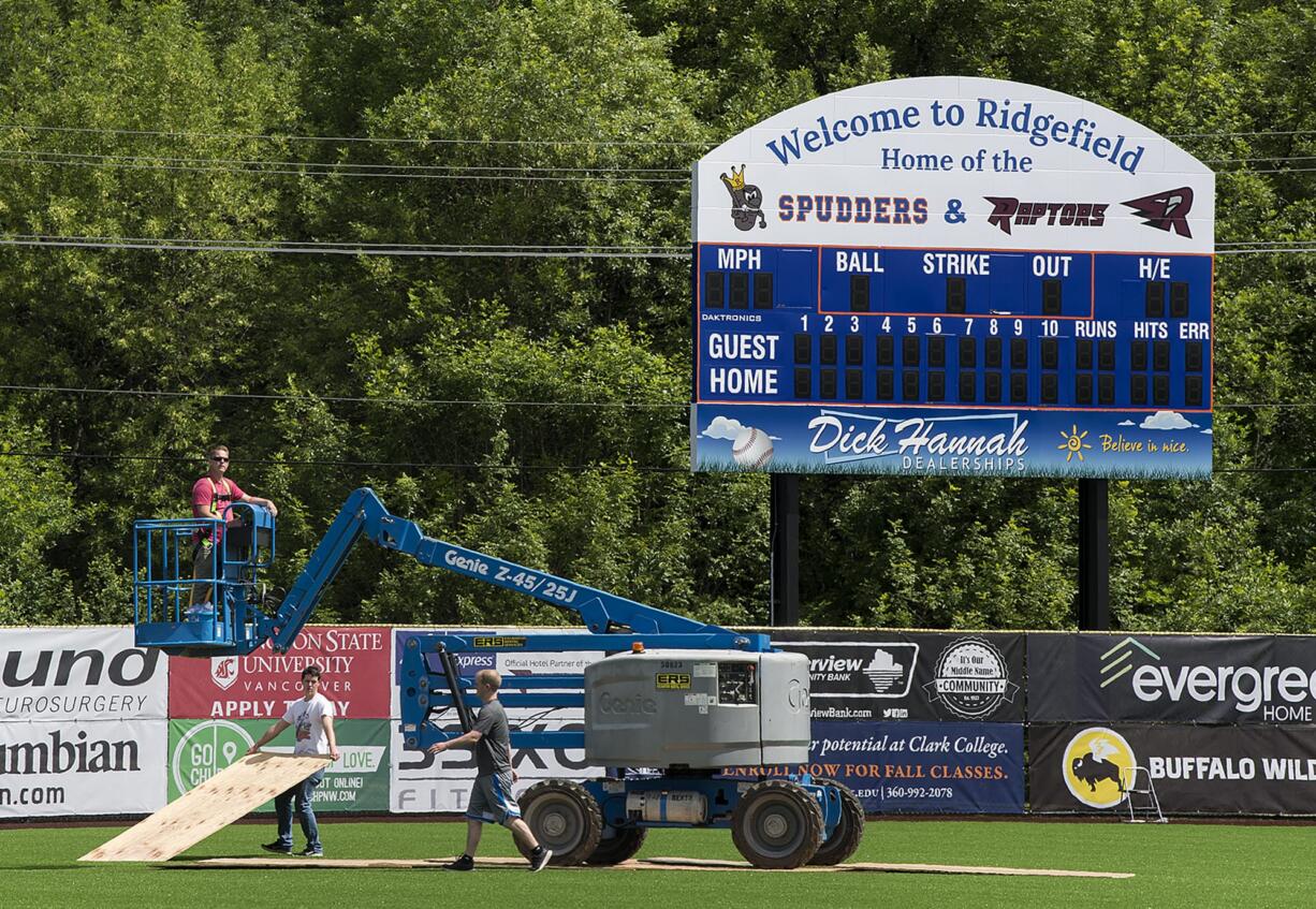 Mike Goldhammer of International Graphics & Nameplate, left, crosses the baseball field at Ridgefield Outdoor Recreation Complex while helping to install banners on the foul poles Monday . Crews put down boards as he crossed to protect the field.