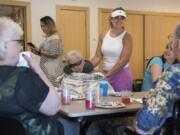 Rita Ulrich, 81, center, and Mera Cosgrove, center right, speak with residents of Magda’s Adult Care during an art show Thursday afternoon at Three Creeks Community Library. Magda’s hosted an art show of the residents’ work and honored recently deceased resident Tauno Alanko.