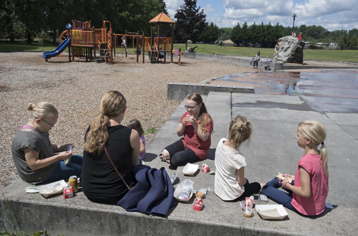 Jodi Massie, 11, center, enjoys some applesauce while joining friends and family as they take part in the summer lunch program at Kiwanis Community Park in Battle Ground on Friday morning. Summer lunch sites are open across Clark County, giving students access to free breakfast, lunch or snacks during the summer months.