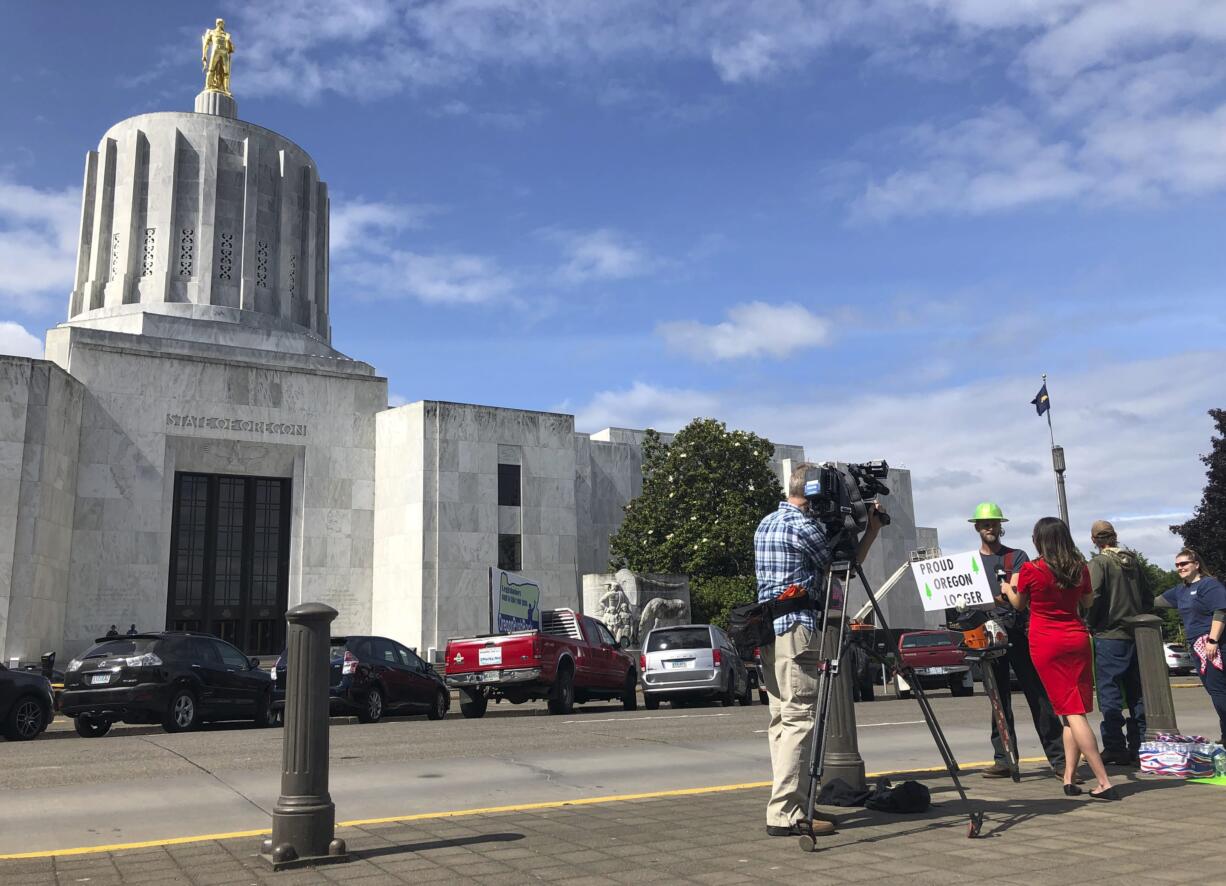 A TV reporter interviews self-employed logger Bridger Hasbrouck, of Dallas, Ore., outside the Oregon State House in Salem, Ore., on Thursday, June 20, 2019, the day the Senate is scheduled to take up a bill that would create the nation's second cap-and-trade program to curb carbon emissions. Senate Republicans, however, pledged to walk out so there wouldn't be enough lawmakers present for a vote on House Bill 2020, which is extremely unpopular among loggers, truckers and many rural voters.