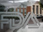 FILE - This Thursday, Aug. 2, 2018, file photo shows the U.S. Food and Drug Administration building behind FDA logos at a bus stop on the agency’s campus in Silver Spring, Md. The Food and Drug Administration’s first broad testing of food for a worrisome class of nonstick, stain-resistant industrial compounds found high levels in some grocery store meats and seafood and in off-the-shelf chocolate cake, according to unreleased findings FDA researchers presented at a scientific conference in Europe.