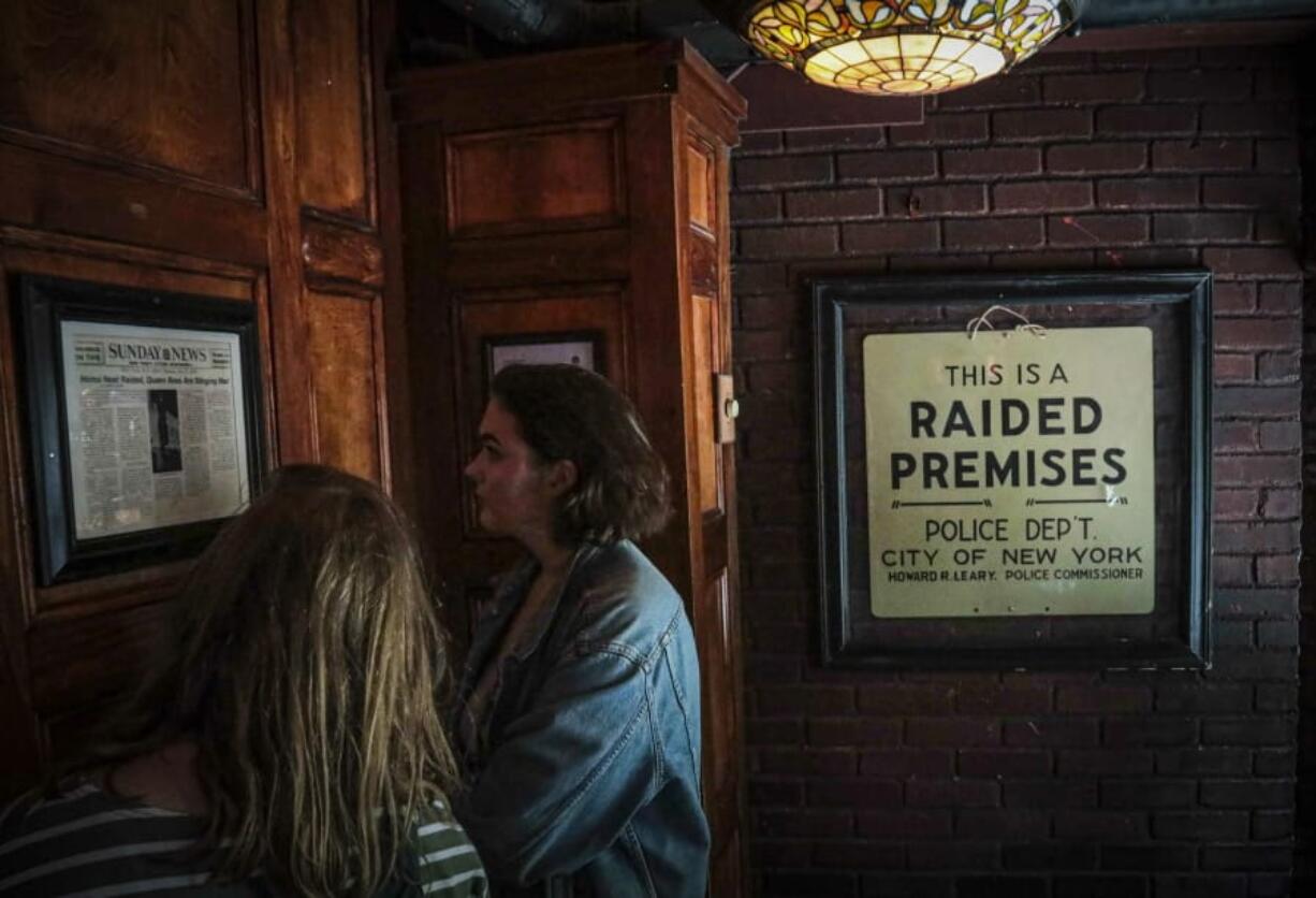 In this Friday June 14, 2019, photo, Stonewall Inn visitors read news clipping headlining the 1969 riots that followed a police raid of the bar in New York.