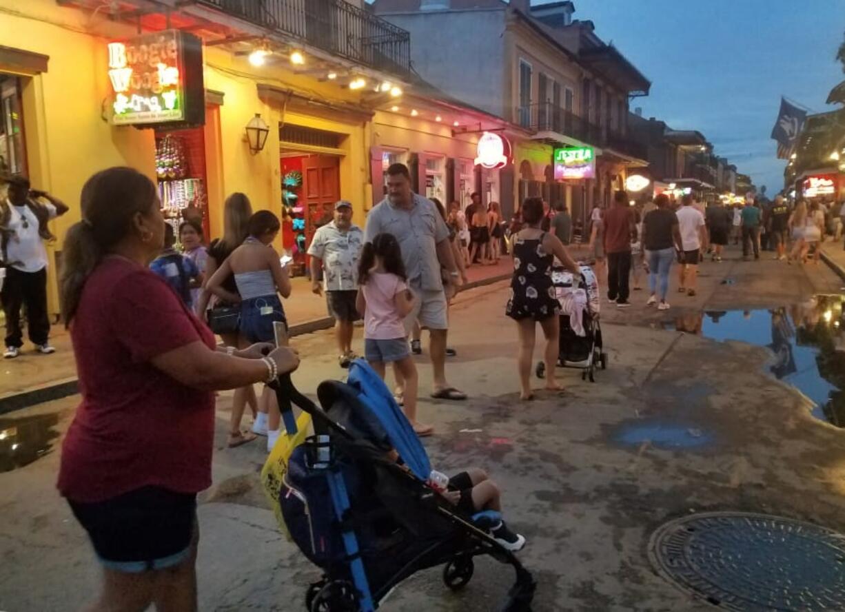 A family walks down Bourbon Street in New Orleans at dusk.