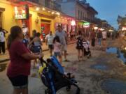 A family walks down Bourbon Street in New Orleans at dusk.