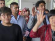 Jalilah Alzeyadi, center, who is originally from Yemen and now lives in Vancouver, joins fellow candidates for citizenship as they take the oath of allegiance during the Special Naturalization Ceremony at the Pearson Air Museum’s historic hangar Wednesday afternoon.