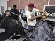 Vancouver resident Samuel Ray, from left, gets a haircut from barber Nard Brown as fellow barber Chaz Davis gives Tobias Adams, 3, his first haircut at CeeDee’z Cutz on June 29. Tobias, who was joined by his family, enjoyed a sucker during the visit to the barbershop, as well as a couple afterward.