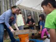 Volunteer Erin Miermans, from left, Evelynn Ramsay, 8, of Vancouver, Rhonin Parks, 8, of Vancouver, Kaitlyn Chan, 6, and her brother, Emlyn Chan, 10, both of Redmond, watch as dirt from the mock archeological dig is sifted Saturday at Fort Vancouver National Historic Site.