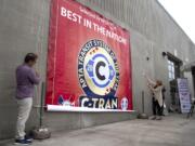 C-Tran Board of Directors member Adrian Cortes, left, and mayor Anne McEnerny-Ogle, right, lower an award announcement during a special event at the C-Tran offices in Vancouver on July 9, 2019. C-Tran revealed that The American Public Transportation Association has selected the company as its Transit System of the Year for 2019.