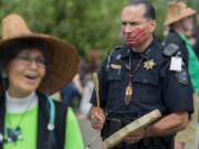 Duane Garvais Lawrence, assistant chief for the tribe’s police department, drums as he waits for canoes to arrive Friday at Marine Park in Vancouver. The red handprint on his face is to raise awareness for missing and murdered indigenous women and girls.