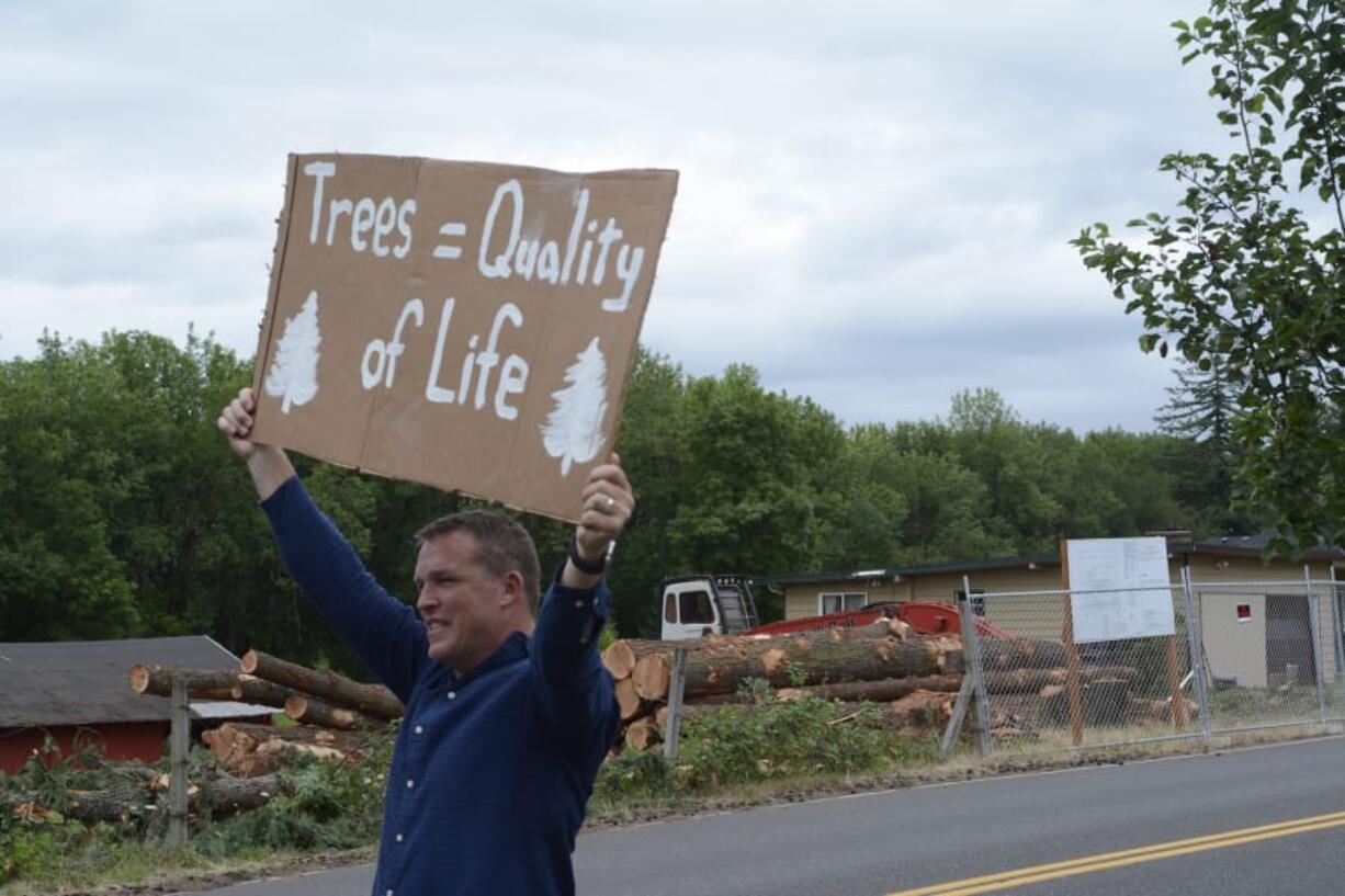 Mike King holds up a sign along Northwest 43rd Avenue in Camas on Wednesday during a protest by the Camas Tree Protectors. The new group hosted the event to protest a developer cutting down nearly 80 trees, some of which can be seen across the street.