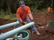 Pete Roberts, foreground, saws into PVC pipe during the installation of a septic tank at a home in Amboy last week. Roberts has owned Bloomquist Septic Inspections since 1997, after spending more than 10 years in the military. He never set out to work in the septic business, and acknowledges that it’s a dirty job.