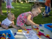 Nine-month-old Haddie Gordon, left, and sister Willow, 3, amuse themselves with Play-Doh on Thursday morning outside the Woodland Community Library during its Sensory Play in the Park event. Library staffers hope they will be able to host more activities for kids and families once the Fort Vancouver Regional Library District raises enough money to construct a bigger building in Woodland.