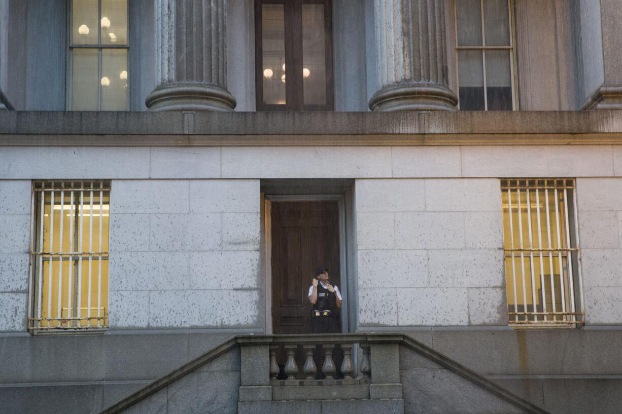 A Uniformed Division Secret Service officer looks up at the rain as he takes shelter in a doorway of the Treasury Building, Monday, July 8, 2019, in Washington.