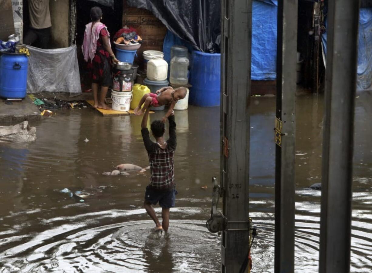 A man holds a child high above his head as he wades through a waterlogged street following heavy rains in Mumbai, India, Tuesday, July 2, 2019. Heavy monsoon rains in western India caused at least three walls to collapse onto huts and city shanties, killing more than two dozen people and injuring dozens of others, officials said Tuesday, as forecasters warned of more rains.