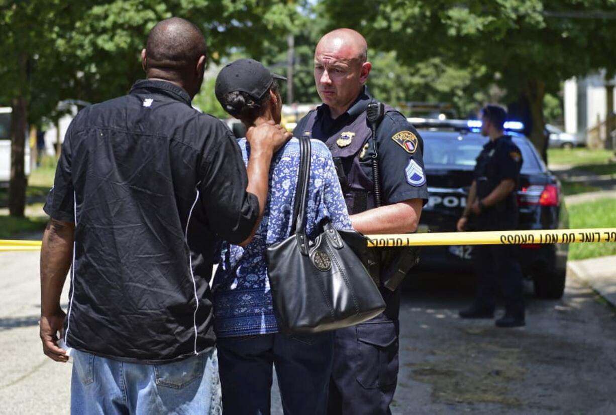 A police officer talks with two bystanders, Tuesday, July 9, 2019, in Cleveland. Police investigating the shooting death of a man in a vacant lot say they also found the bodies of a woman and two children in a nearby house. Authorities aren’t saying how the three found inside the house Tuesday died, but they did say the four deaths are connected.