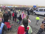 Police in riot gear are lined up on a road in Hawaii where an estimated 2,000 people are gathered to protest construction of a telescope on a mountain that some Native Hawaiians consider sacred, on Mauna Kea on the Big Island of Hawaii, Wednesday, July 17, 2019. Hawaii County Managing Director Wil Okabe says officials on Wednesday closed a highway leading to the protest site so a convoy of construction equipment can be brought up Mauna Kea. Protesters are off to the side of the road, singing.