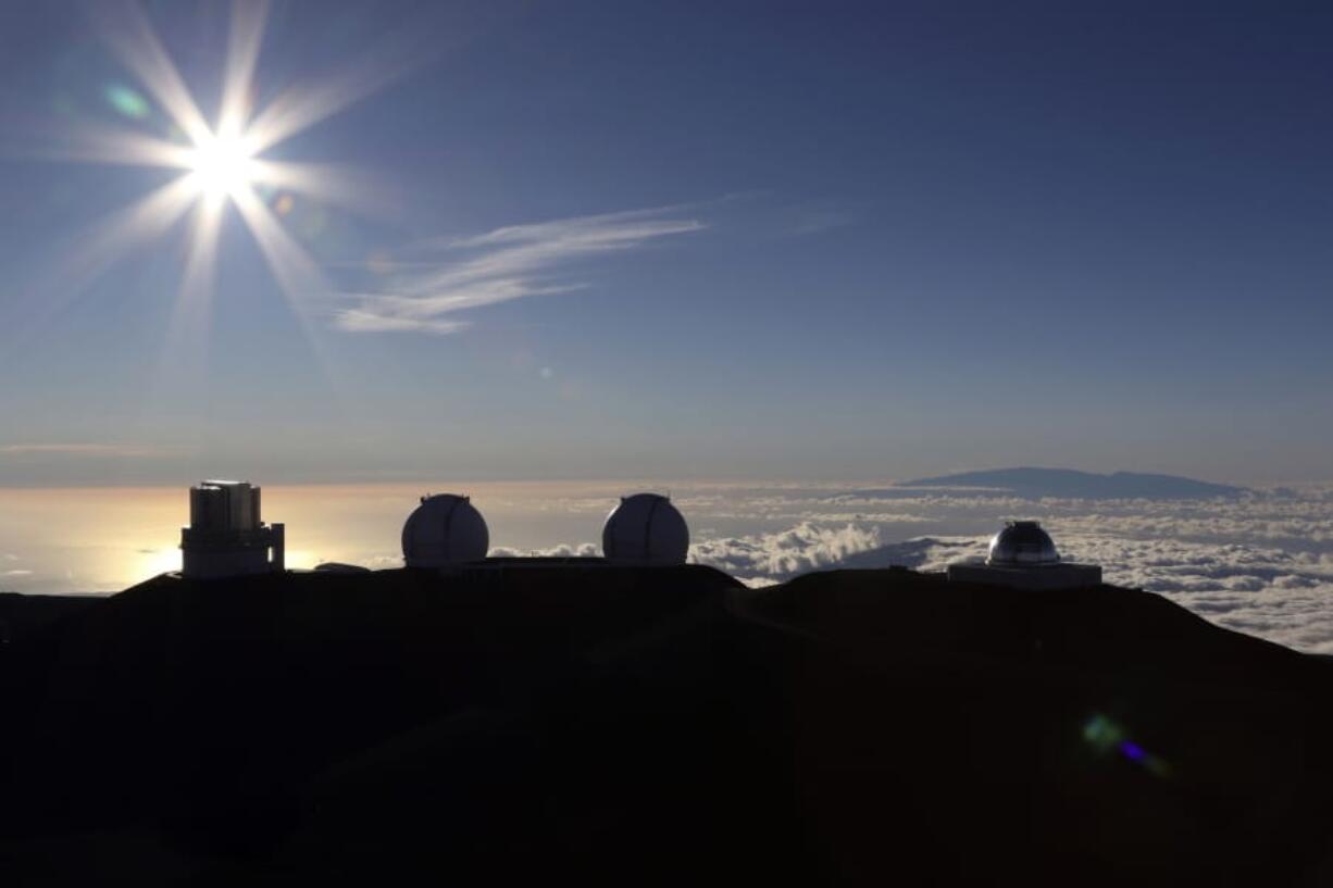 FILE - In this Sunday, July 14, 2019, file photo, the sun sets behind telescopes at the summit of Mauna Kea. Scientists are expected to explore fundamental questions about our universe when they use a giant new telescope planned for the summit of Hawaii’s tallest mountain. That includes whether there’s life outside our solar system and how stars and galaxies formed in the earliest years of the universe. But some Native Hawaiians don’t want the Thirty Meter Telescope to be built at Mauna Kea’s summit, saying it will further harm a place they consider sacred.