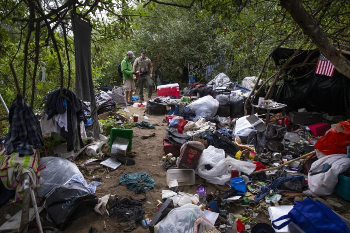 Ambassador Joe Waksmundski, left, and Lane County Sheriff’s Deputy Justin Bond visit a campsite Tuesday on an island just downstream from the Ferry Street Bridge that is littered with trash, needles and other debris left behind by people using the spot as a place to live, in Eugene, Ore. City of Eugene Public Works, Park and Open Space staff and a Lane County Jail work crew teamed up to clean up the site.