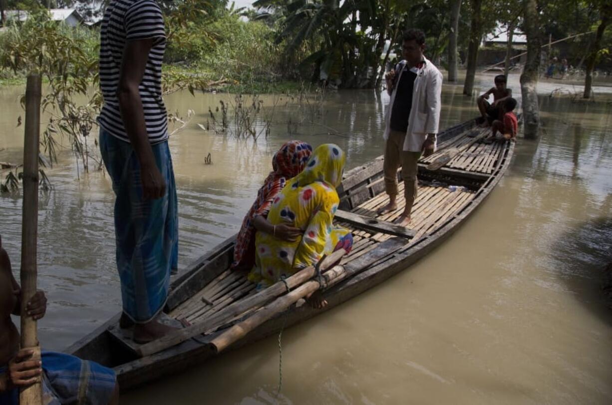 In this Friday, July 19, 2019 photo, Imrana Khatoon, in yellow, leaves her home on a boat to get to a hospital, as a woman sits beside her holding Khatoon’s newborn baby, in flood-affected Gagalmari, east of Gauhati, India. Khatoon, 20, delivered her first baby on a boat in floodwaters early Friday while on her way to a hospital, locals said. The woman and the newborn were brought back to their home without getting to hospital. They were however moved to a hospital on a boat to the nearby Jhargaon town because of unhygienic conditions due to floodwaters, Community health worker Parag Jyoti Das said.