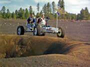 This undated photo provided by the U.S. Geological Survey Astrogeology Science Center shows Apollo 15 astronauts Jim Irwin, left, and Dave Scott driving a prototype of a lunar rover in a volcanic cinder field east of Flagstaff, Ariz. The rover, named Grover, now is on display at the science center. (U.S.