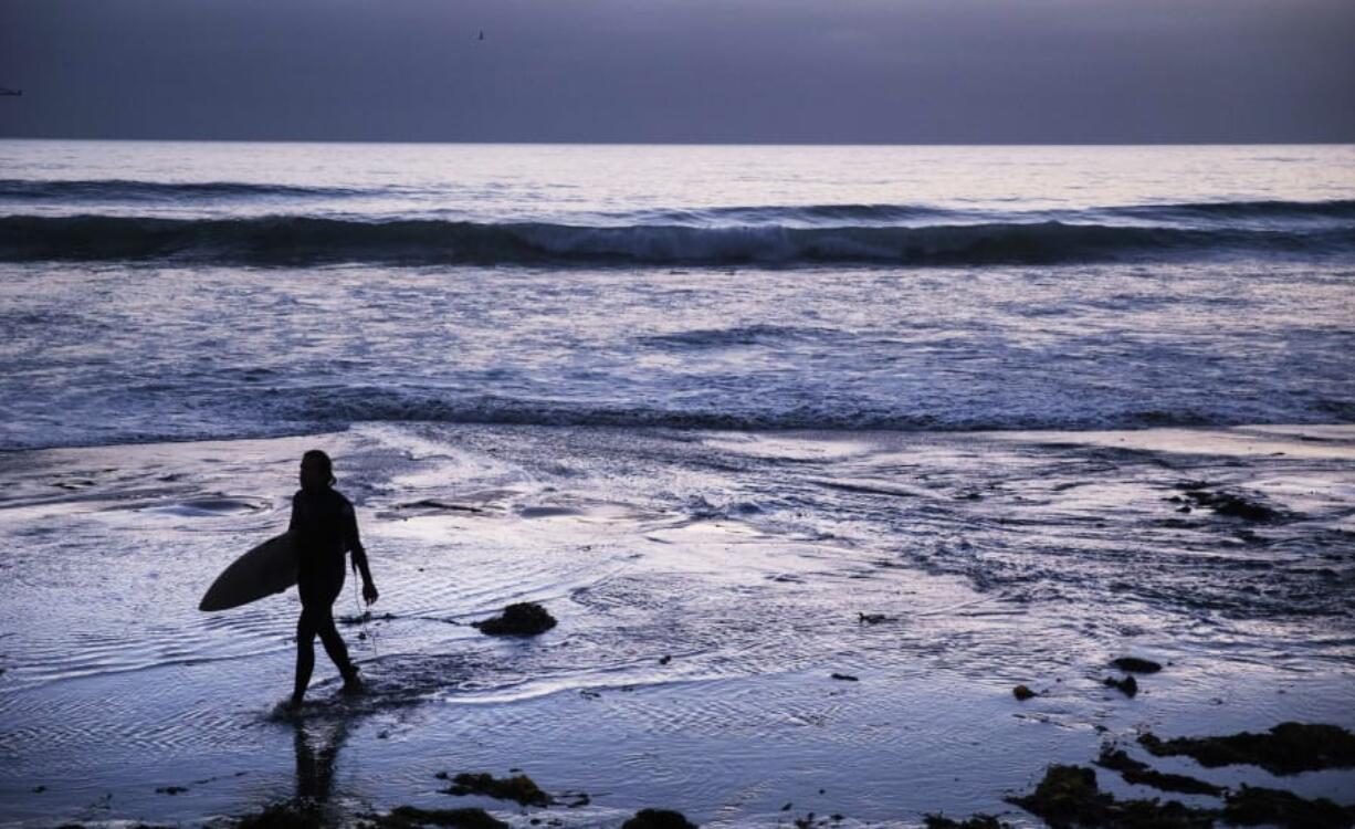 In this July 2 file photo, a surfer walks out of the water after riding waves at dusk at Scripps Beach in San Diego. With hotel and airline loyalty programs, you can take the sting out of this year’s travel costs by leveraging those expenditures to pay for next year’s trip.