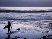 In this July 2 file photo, a surfer walks out of the water after riding waves at dusk at Scripps Beach in San Diego. With hotel and airline loyalty programs, you can take the sting out of this year’s travel costs by leveraging those expenditures to pay for next year’s trip.