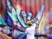 Nathan Howard/The Columbian Spray paint artist “FABS” (Camille Cote) adds final touches to a mural on a shipping container at the back of a parking lot on Fourth Plain Boulevard.