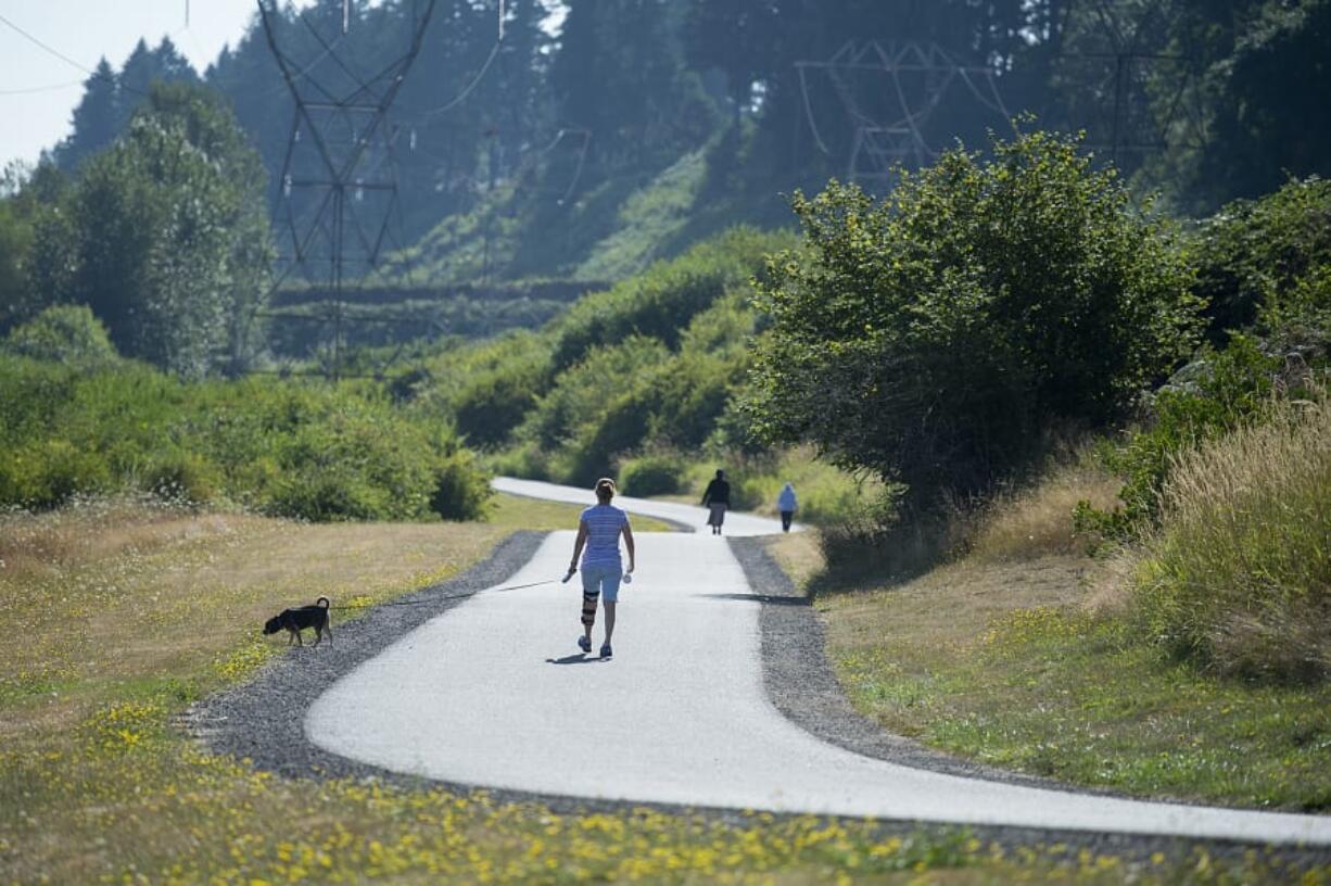 Pedestrians stroll on a paved path near a restored section of the Burnt Bridge Creek greenway Wednesday morning. The path is near where the city eliminated reed canary grass and other invasive species and replaced it with native trees and other vegetation.