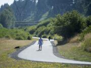 Pedestrians stroll on a paved path near a restored section of the Burnt Bridge Creek greenway Wednesday morning. The path is near where the city eliminated reed canary grass and other invasive species and replaced it with native trees and other vegetation.