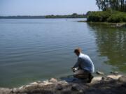 Clark County Public Health intern Michael Wagner collects a water sample for cyanotoxin level testing in the flushing channel at Vancouver Lake. The Washington Department of Ecology pays for the testing, and the samples are shipped overnight to King County Environmental Lab. Testing results from Monday’s collection could return today. At top, signs are posted to warn visitors that the lake is closed.