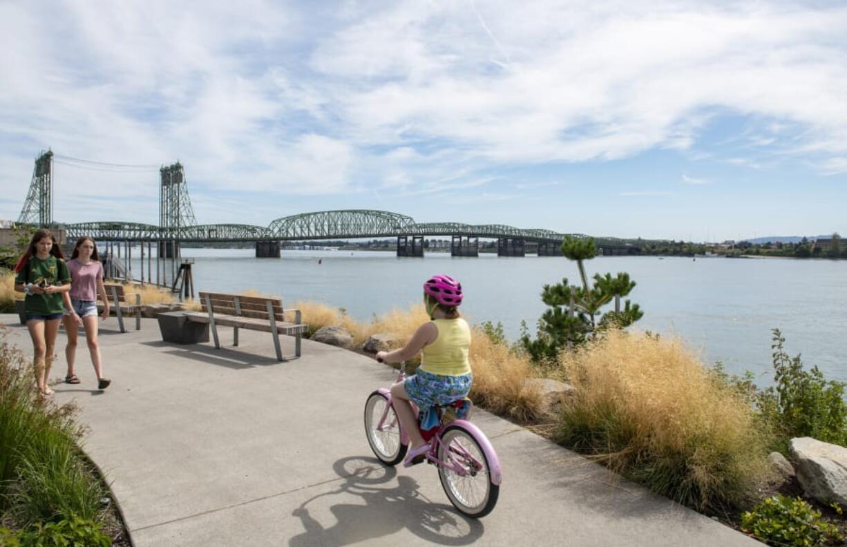 Jaidyn Geesey, left, and Ava Soucy stroll along the Columbia River at Vancouver Waterfront Park on Wednesday afternoon. The Interstate 5 Bridge, which both states want to replace, spans the Columbia River behind them.