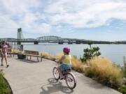 Jaidyn Geesey, left, and Ava Soucy stroll along the Columbia River at Vancouver Waterfront Park on Wednesday afternoon. The Interstate 5 Bridge, which both states want to replace, spans the Columbia River behind them.