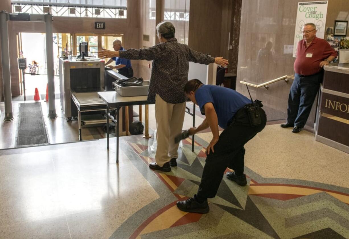 Courthouse security officer Brian Aranda, middle right, uses a hand-held metal detector on a visitor, while information desk volunteer Bob Weller, right, waits at his desk at the Clark County Courthouse on Thursday morning.