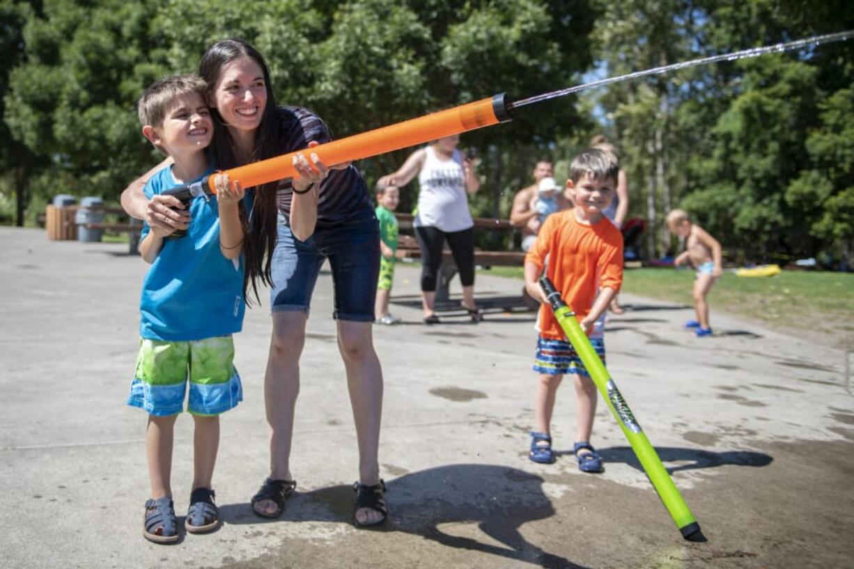 Matthew Lowenstein, 7, left, and his mother Amber, center, spray a water soaker, while his brother Mark, 5, right, watches Tuesday afternoon at Klineline Pond in Vancouver.