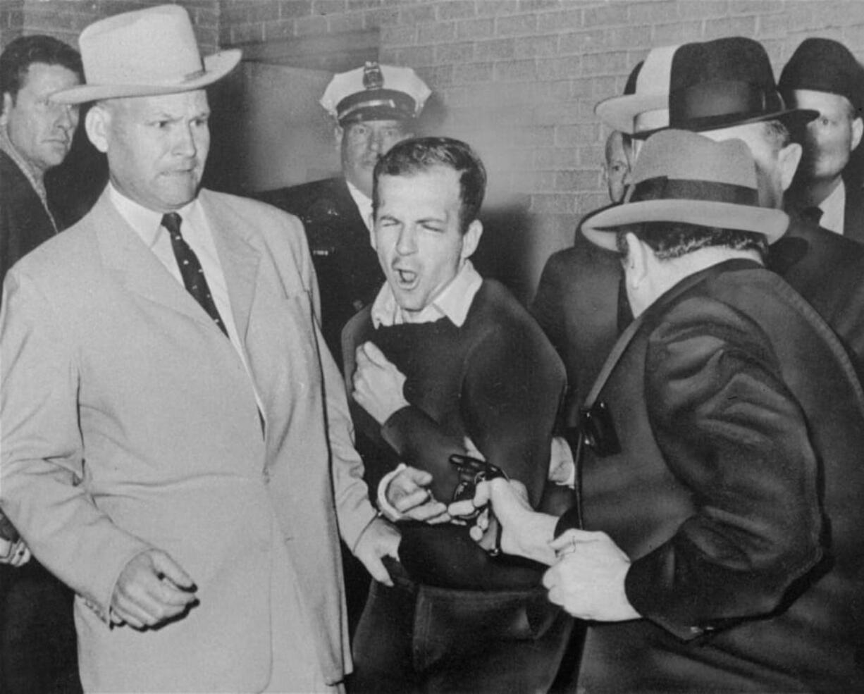 FILE - In this Nov. 24, 1963 file photo, Lee Harvey Oswald reacts as Dallas night club owner Jack Ruby, foreground, shoots at him from point blank range in a corridor of Dallas police headquarters At left is Detective Jim Leavelle. The longtime Dallas lawman who was captured in one of history’s most iconic photographs as he escorted President John F. Kennedy’s assassin moments before he was fatally shot, has died on Thursday, Aug. 29, 2019. He was 99.