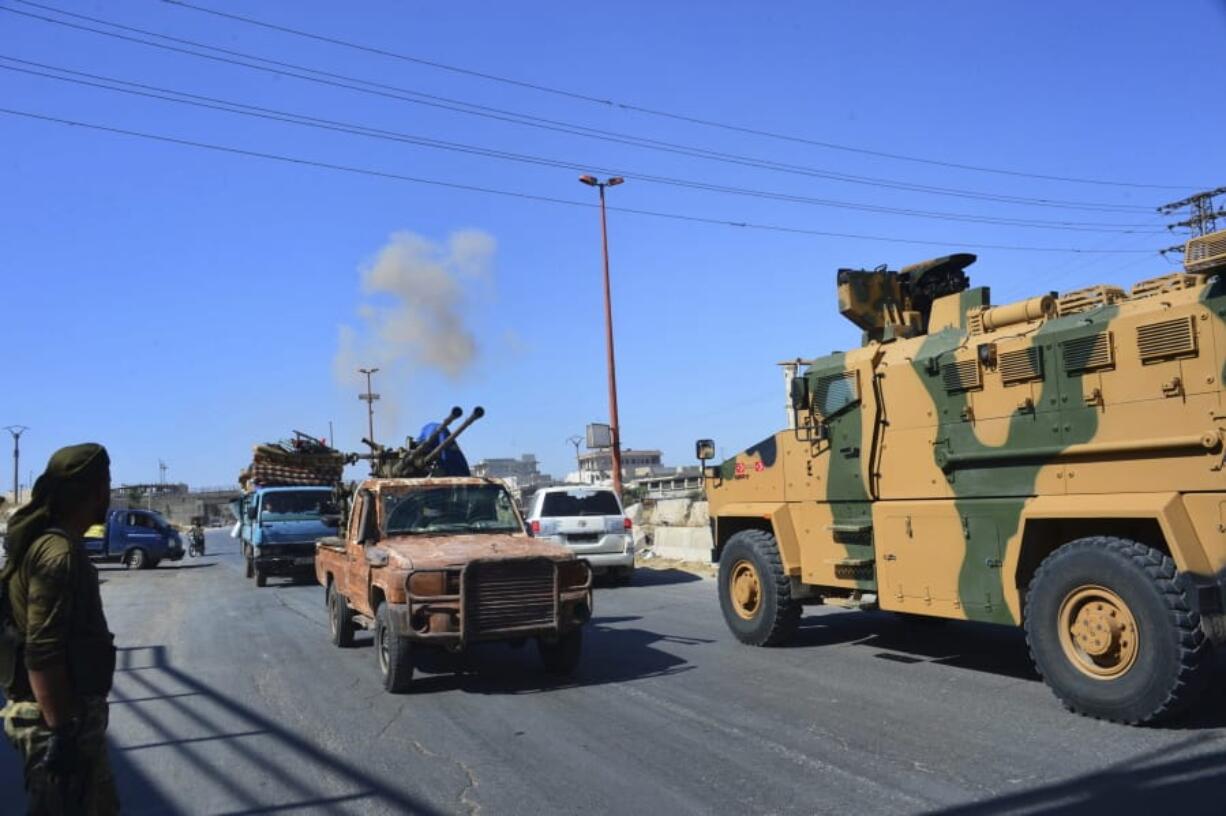 Smoke rises in the background from bombardment around the area as fighters with the Free Syrian army drive their pick-up truck, left, past a Turkey Armed Forces convoy, at a highway between Maaret al-Numan and Khan Sheikhoun in Idlib province, Syria, Monday, Aug. 19, 2019. The Turkish Defense Ministry says airstrikes have targeted a Turkish military convoy in Syria, killing at least three civilians and wounding 12 others in Monday’s attack that occurred while the convoy was heading toward a Turkish observation post in the rebel-held stronghold of Idlib.