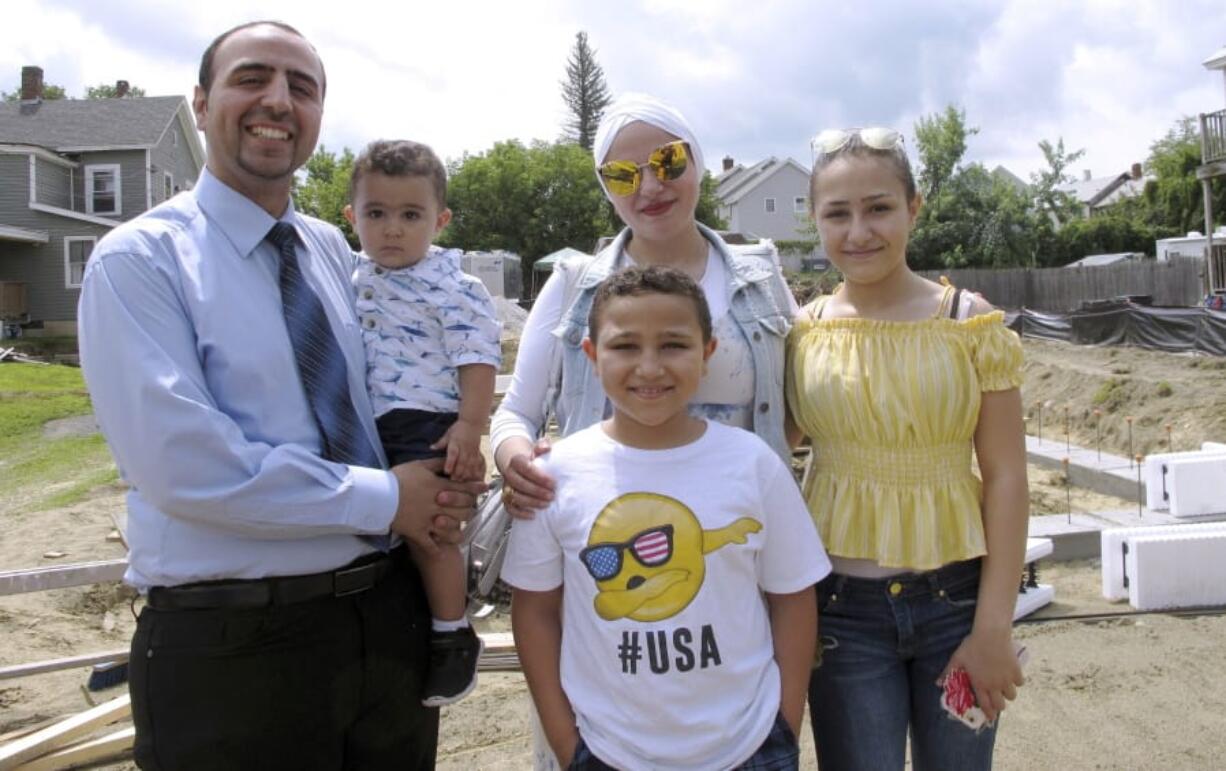 In this July 31, 2019 photo, Hussam Alhallak, left, sons Danyal, held by his father, and Muhammad, wife Hazar Mansour and daughter Layan, right, stand at the site of their new home being built by Habitat for Humanity of Rutland County in Rutland, Vt. The family fled the war in Syria and are making a life for themselves in Vermont.