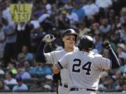 A fan holds a sign that reads “All Rise” as New York Yankees’ Aaron Judge, left, greets Gary Sanchez (24) after Judge hit a two-run home run against the Seattle Mariners during the fifth inning of a baseball game, Wednesday, Aug. 28, 2019, in Seattle. (AP Photo/Ted S.