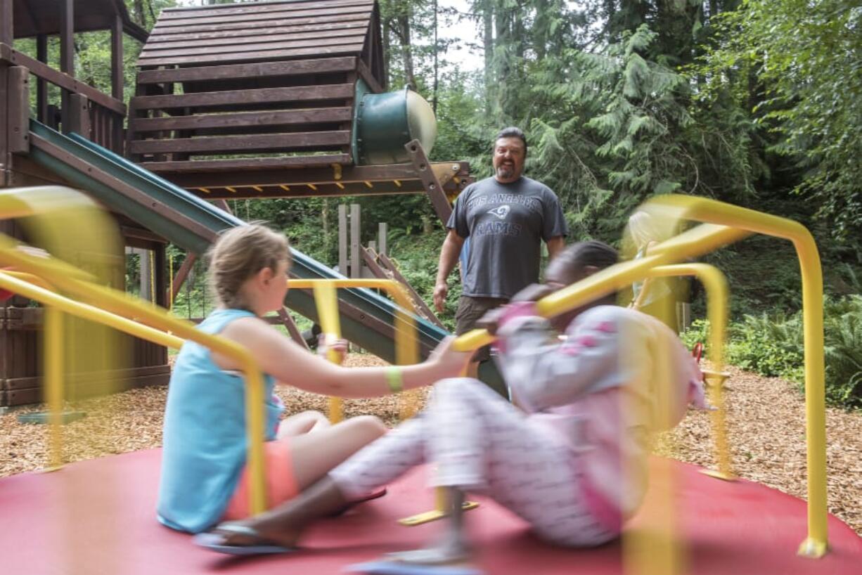 Ron Darland, center, watches as foster children play at Alderbrook Park during a Mockingbird event on July 27. Top: Connie Ryley, left, and Laura Darland go through the medication schedule of two foster kids that Ryley dropped off at the Darland home on July 22 before leaving on vacation. Respite is a major part of the Mockingbird Family Model of foster care.