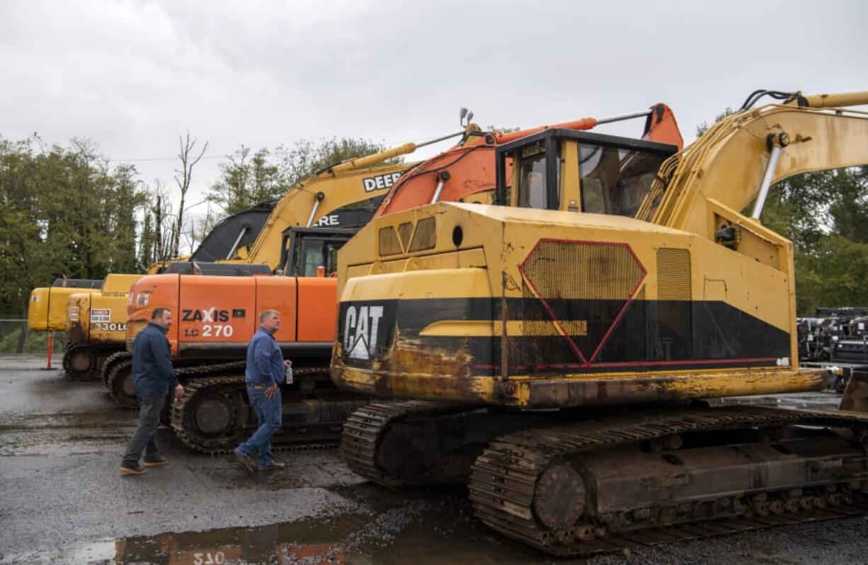 Robertson & Olson fleet manager Darin Borg, left, and owner Matt Olson, right, look at a row of excavators at the new J. Stout Auctions facility in Washougal on Tuesday.