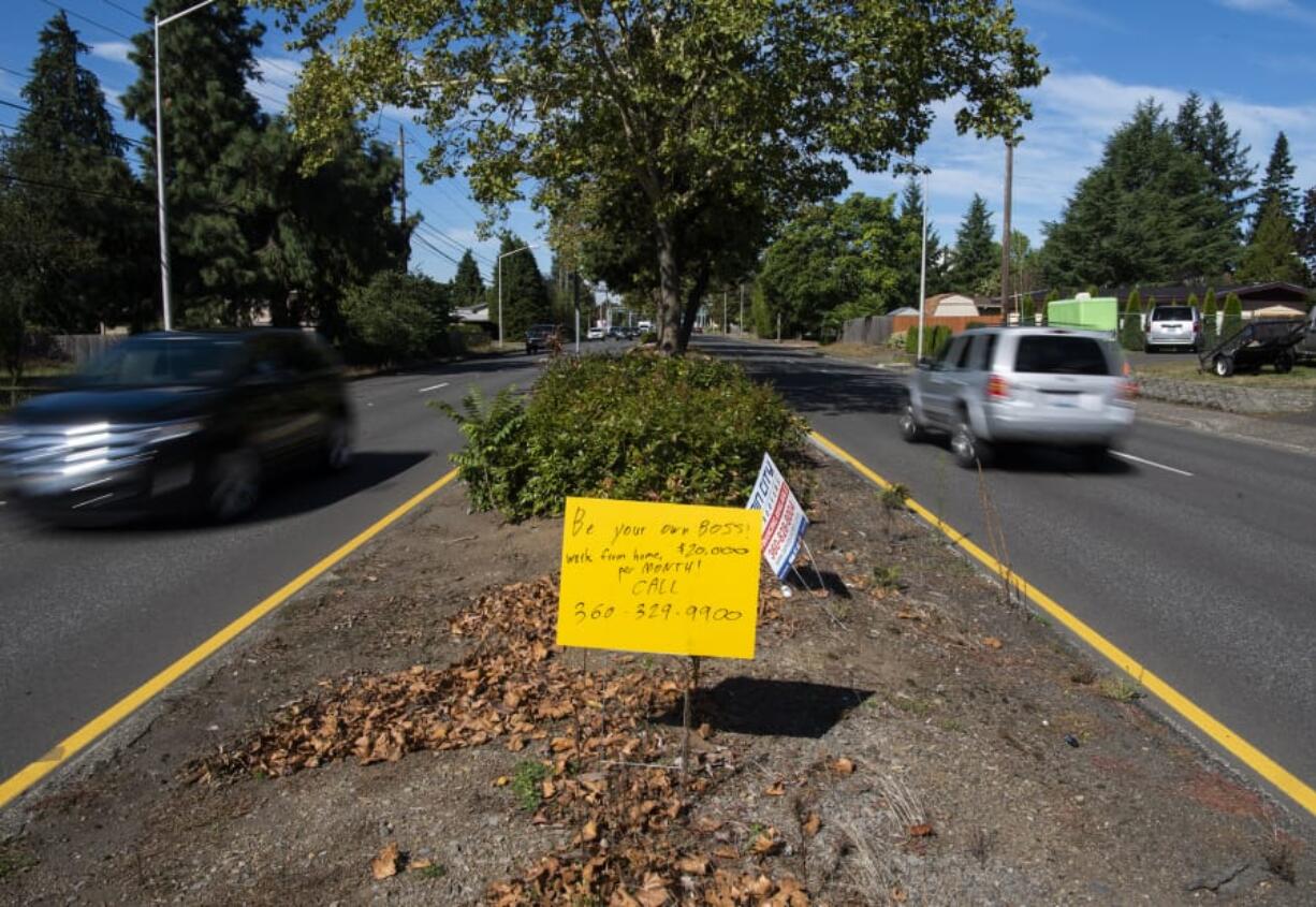 A hand-scrawled sign promising people $20,000 per month for working at home stands in the median along Mill Plain Boulevard near PeaceHealth Southwest Medical Center in Vancouver.