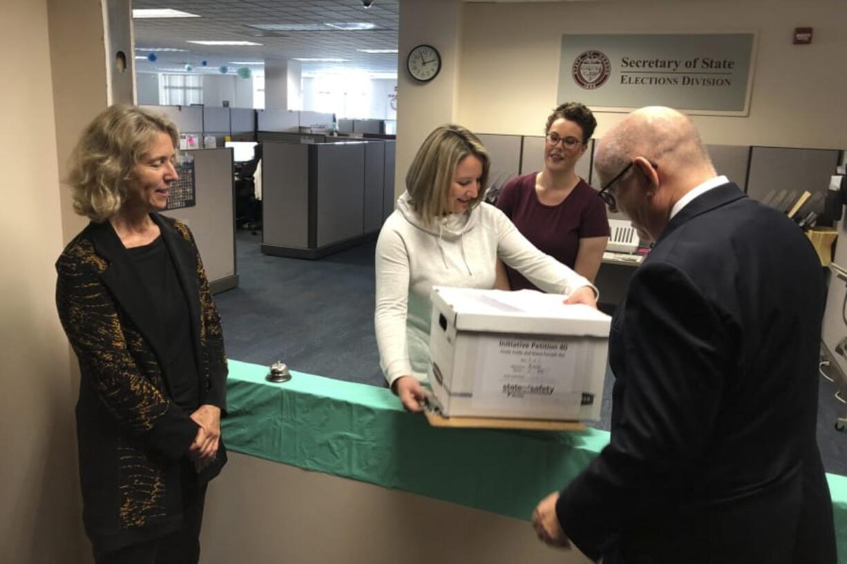 Lydia Plukchi of the Oregon Secretary of State&#039;s office in Salem, Ore., accepts on Wednesday, Sept. 18, 2019, a box containing 2,000 signatures backing a proposed ballot measure that would create the most comprehensive law in America requiring the safe storage of weapons, as worker Amanda Kessel, behind her, looks on. Delivering the box are Henry Wessinger, president of the State of Safety Action which is backing the proposed measure, and Rep. Alissa Keny-Guyer.