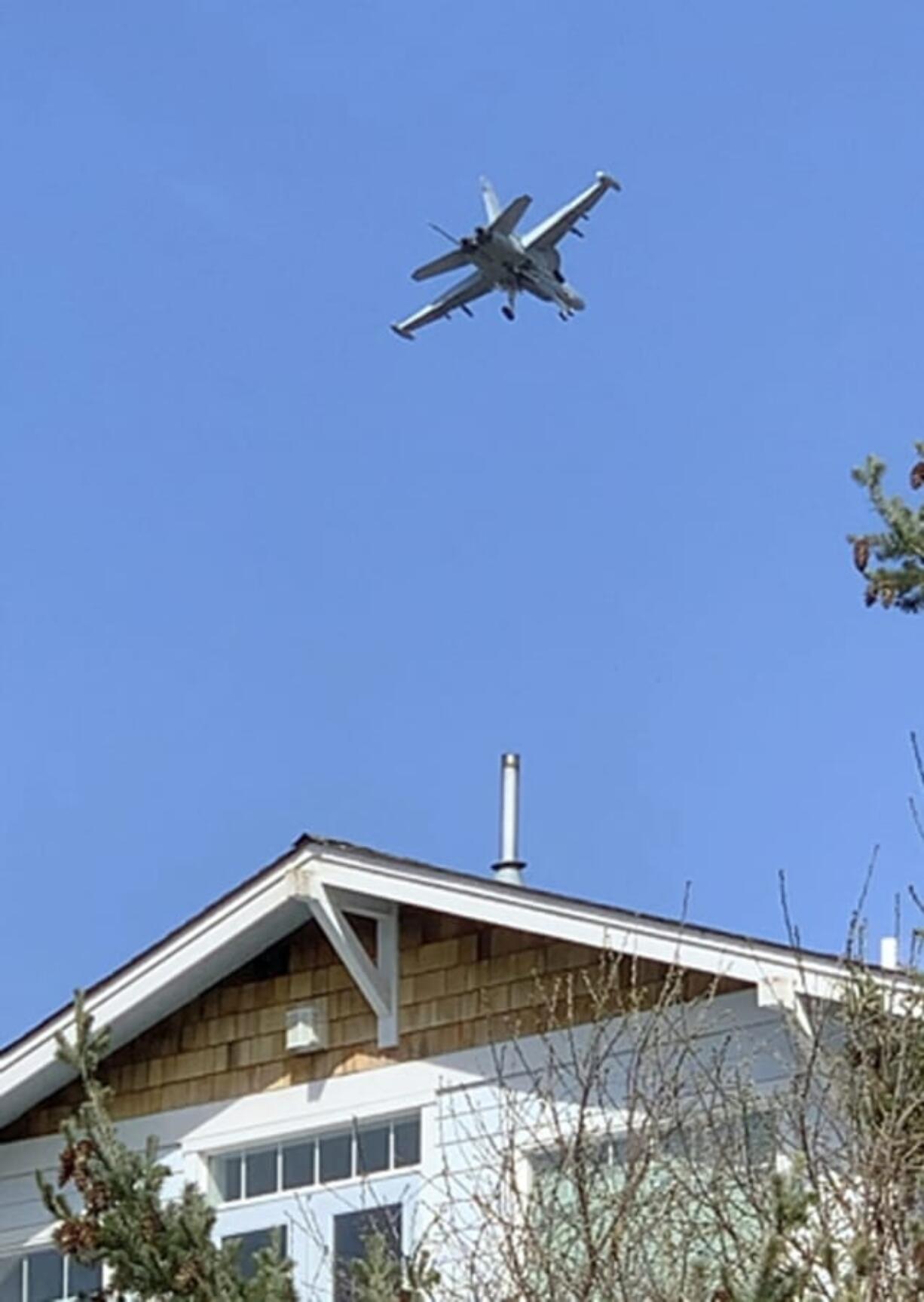 This March 28, 2019 photo from video provided by Whidbey Island resident Bradley Portin shows a Navy jet roaring above the home of his neighbors Marge Plecki and Michael King in Coupeville, Wash. Portin, Plecki and King are among three dozen residents who filed a federal lawsuit against the Navy last week, saying the incessant noise from expanded flight training operations at a small nearby landing strip have cost them the use of their properties and made their lives miserable.